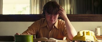 Movie still from “Licorice Pizza” (2021), directed by Paul Thomas Anderson – A man sitting at a table with a book in front of him; Close Up shot, Low angle