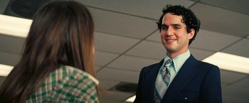 Movie still from “Licorice Pizza” (2021), directed by Paul Thomas Anderson – A man wearing a suit and tie standing next to a woman; Close Up shot, Over the shoulder angle