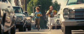 Movie still from “Licorice Pizza” (2021), directed by Paul Thomas Anderson – Two women walking down the street holding papers; Wide shot, High angle