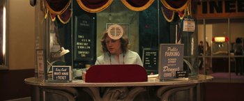 Movie still from “Licorice Pizza” (2021), directed by Paul Thomas Anderson – A woman sitting at a counter in front of a window; Medium shot, Over the shoulder angle
