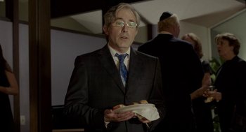 Movie still from “Life After Beth” (2014), directed by Jeff Baena – A man in a suit and tie holding a sandwich; Medium shot, Over the shoulder angle