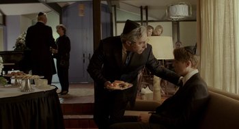 Movie still from “Life After Beth” (2014), directed by Jeff Baena – A man in a suit holding a plate of food in his hand; Medium shot, Over the shoulder angle