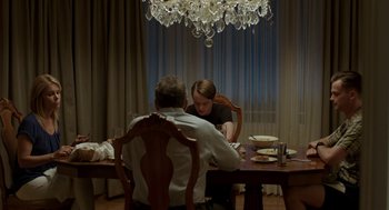 Movie still from “Life After Beth” (2014), directed by Jeff Baena – Two people sitting at a dinner table in front of chandeliers; Medium shot, Over the shoulder angle