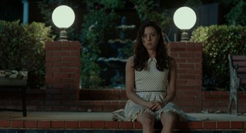 Movie still from “Life After Beth” (2014), directed by Jeff Baena – A woman sitting on a brick wall in front of a fountain; Medium shot, High angle