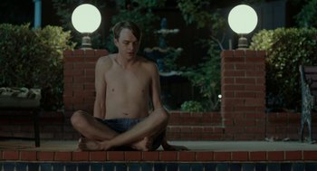 Movie still from “Life After Beth” (2014), directed by Jeff Baena – A man sitting on a brick wall in front of a pool; Medium shot, High angle