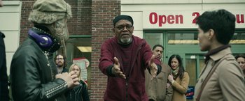 Movie still from “Life Itself” (2018), directed by Dan Fogelman – An older man is holding his hands out in front of a crowd of onlookers; Medium shot, Low angle