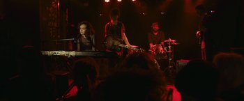 Movie still from “Life Itself” (2018), directed by Dan Fogelman – A group of people sitting on a stage playing instruments; Wide shot, High angle