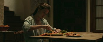 Movie still from “Life Itself” (2018), directed by Dan Fogelman – A woman cutting vegetables on a cutting board on top of a wooden table; Medium shot, Over the shoulder angle
