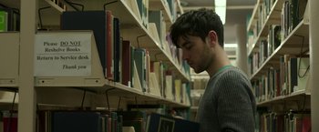 Movie still from “Life Itself” (2018), directed by Dan Fogelman – A young man is looking at books in a library; Close Up shot, High angle