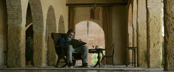 Movie still from “Life Itself” (2018), directed by Dan Fogelman – An older man sitting in a chair reading a book; Wide shot, Low angle