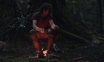 Movie still from “Light of My Life” (2019), directed by Casey Affleck – A man sitting on the ground near a fire pit; Wide shot, Low angle