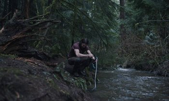 Movie still from “Light of My Life” (2019), directed by Casey Affleck – A man in the woods holding onto a water hose; Wide shot, Low angle