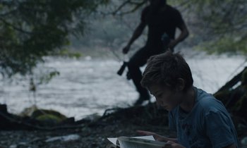 Movie still from “Light of My Life” (2019), directed by Casey Affleck – A young boy sitting on the ground near a body of water; Medium shot, Over the shoulder angle