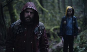 Movie still from “Light of My Life” (2019), directed by Casey Affleck – A man in a red jacket and a woman in a yellow jacket walking through the woods; Medium shot, Over the shoulder angle