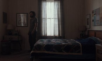 Movie still from “Light of My Life” (2019), directed by Casey Affleck – A man standing next to a bed in front of a window; Wide shot, High angle