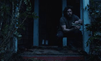 Movie still from “Light of My Life” (2019), directed by Casey Affleck – A man sitting on the steps of a house holding a book; Medium shot, Low angle