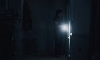 Movie still from “Light of My Life” (2019), directed by Casey Affleck – A man standing in a dark room holding a flashlight; Medium shot, Low angle