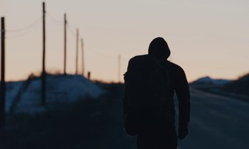 Movie still from “Light of My Life” (2019), directed by Casey Affleck – A person with a backpack walking on a road; Wide shot, Low angle