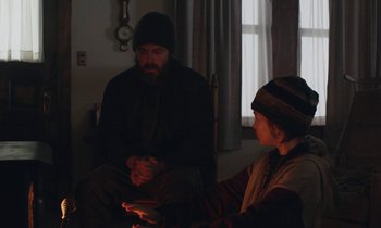Movie still from “Light of My Life” (2019), directed by Casey Affleck – A man sitting next to a child in a living room; Medium shot, Over the shoulder angle