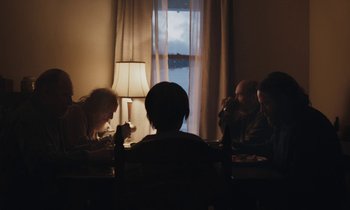 Movie still from “Light of My Life” (2019), directed by Casey Affleck – A group of people sitting around a table at night; Wide shot, Over the shoulder angle
