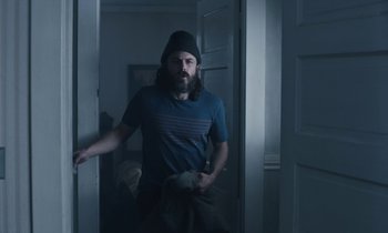Movie still from “Light of My Life” (2019), directed by Casey Affleck – A man in a blue shirt and a black hat standing in front of a door; Medium shot, Low angle