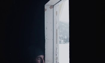 Movie still from “Light of My Life” (2019), directed by Casey Affleck – A man is looking out of a window at a snowy mountain; Medium shot, High angle