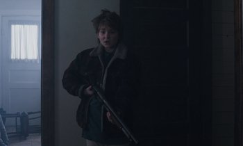 Movie still from “Light of My Life” (2019), directed by Casey Affleck – A young boy holding a rifle in a dark room; Medium shot, Low angle