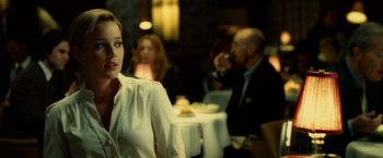 Movie still from “Limitless” (2011), directed by Neil Burger – A woman sitting at a table in front of people; Medium shot, Over the shoulder angle