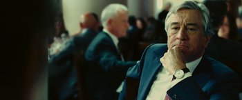 Movie still from “Limitless” (2011), directed by Neil Burger – A man in a suit sitting in front of other people; Close Up shot, Over the shoulder angle