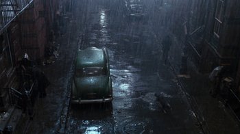 Movie still from “Little Shop of Horrors” (1986), directed by Frank Oz – An old car is parked in the middle of the street in the pouring rain; Extreme Wide shot, Overhead angle