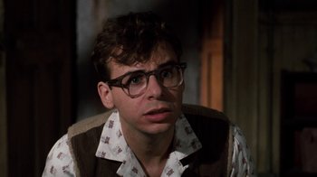 Movie still from “Little Shop of Horrors” (1986), directed by Frank Oz – A young man wearing glasses sitting in a chair; Close Up shot, Low angle