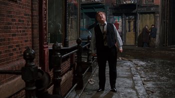 Movie still from “Little Shop of Horrors” (1986), directed by Frank Oz – A man in a vest and tie standing on a sidewalk; Wide shot, Over the shoulder angle