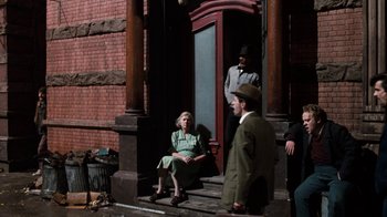 Movie still from “Little Shop of Horrors” (1986), directed by Frank Oz – An older woman sitting on the steps of a building; Wide shot, Over the shoulder angle