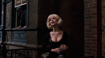 Movie still from “Little Shop of Horrors” (1986), directed by Frank Oz – A woman in a black dress is standing by a window; Medium shot, Low angle