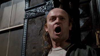 Movie still from “Little Shop of Horrors” (1986), directed by Frank Oz – A man with long hair and a bald head is looking surprised; Close Up shot, Low angle