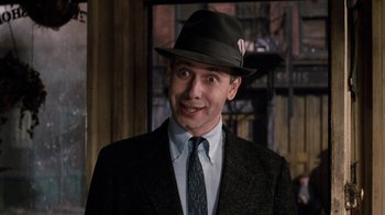 Movie still from “Little Shop of Horrors” (1986), directed by Frank Oz – A man wearing a suit and a hat smiling for the camera; Close Up shot, Over the shoulder angle