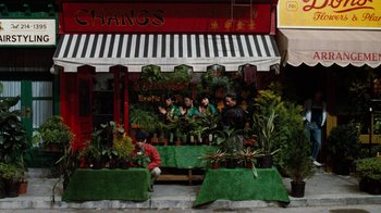 Movie still from “Little Shop of Horrors” (1986), directed by Frank Oz – A group of people sitting in front of a plant shop; Extreme Wide shot, Overhead angle