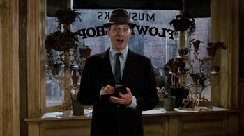 Movie still from “Little Shop of Horrors” (1986), directed by Frank Oz – A man in a suit and hat holding a cell phone; Medium shot, Low angle