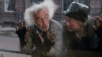 Movie still from “Little Shop of Horrors” (1986), directed by Frank Oz – A man with white hair and a man with grey hair and a black hat; Medium shot, Overhead angle