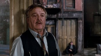 Movie still from “Little Shop of Horrors” (1986), directed by Frank Oz – An older man wearing a vest and a tie; Medium shot, Over the shoulder angle