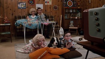 Movie still from “Little Shop of Horrors” (1986), directed by Frank Oz – A group of people sitting in a room with a dog; Wide shot, High angle