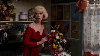 Movie still from “Little Shop of Horrors” (1986), directed by Frank Oz – A woman in a red dress standing in front of flowers; Medium shot, Over the shoulder angle
