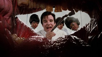 Movie still from “Little Shop of Horrors” (1986), directed by Frank Oz – A group of people standing in front of an open mouth; Extreme Close Up shot, Low angle