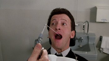 Movie still from “Little Shop of Horrors” (1986), directed by Frank Oz – A man in a black suit holding a syringe in his mouth; Close Up shot, Overhead angle