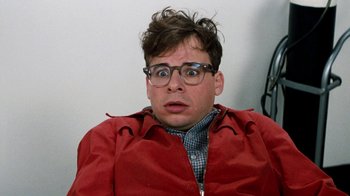 Movie still from “Little Shop of Horrors” (1986), directed by Frank Oz – A man in a red jacket with glasses; Close Up shot, Low angle