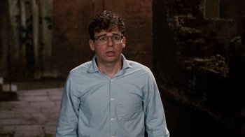 Movie still from “Little Shop of Horrors” (1986), directed by Frank Oz – A man in a blue shirt and glasses is looking at the camera; Medium shot, Over the shoulder angle