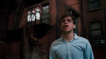 Movie still from “Little Shop of Horrors” (1986), directed by Frank Oz – A man standing in front of a brick building; Medium shot, Low angle