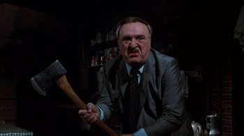 Movie still from “Little Shop of Horrors” (1986), directed by Frank Oz – A man in a suit holding an axe in a dark room; Close Up shot, Low angle