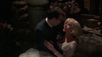 Movie still from “Little Shop of Horrors” (1986), directed by Frank Oz – A man and a woman are sitting in a dark room; Medium shot, High angle