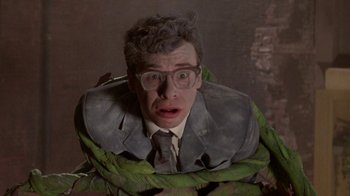 Movie still from “Little Shop of Horrors” (1986), directed by Frank Oz – A man in a suit and tie with a surprised look on his face; Medium shot, Overhead angle